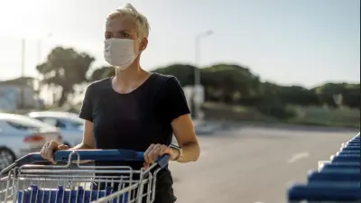 Woman wearing a face mask using a shopping trolley walking to a store
