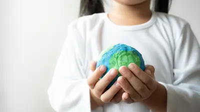 Close-up of a young child in a white shirt holding a small globe with both hands, symbolizing care for the Earth and sustainability.